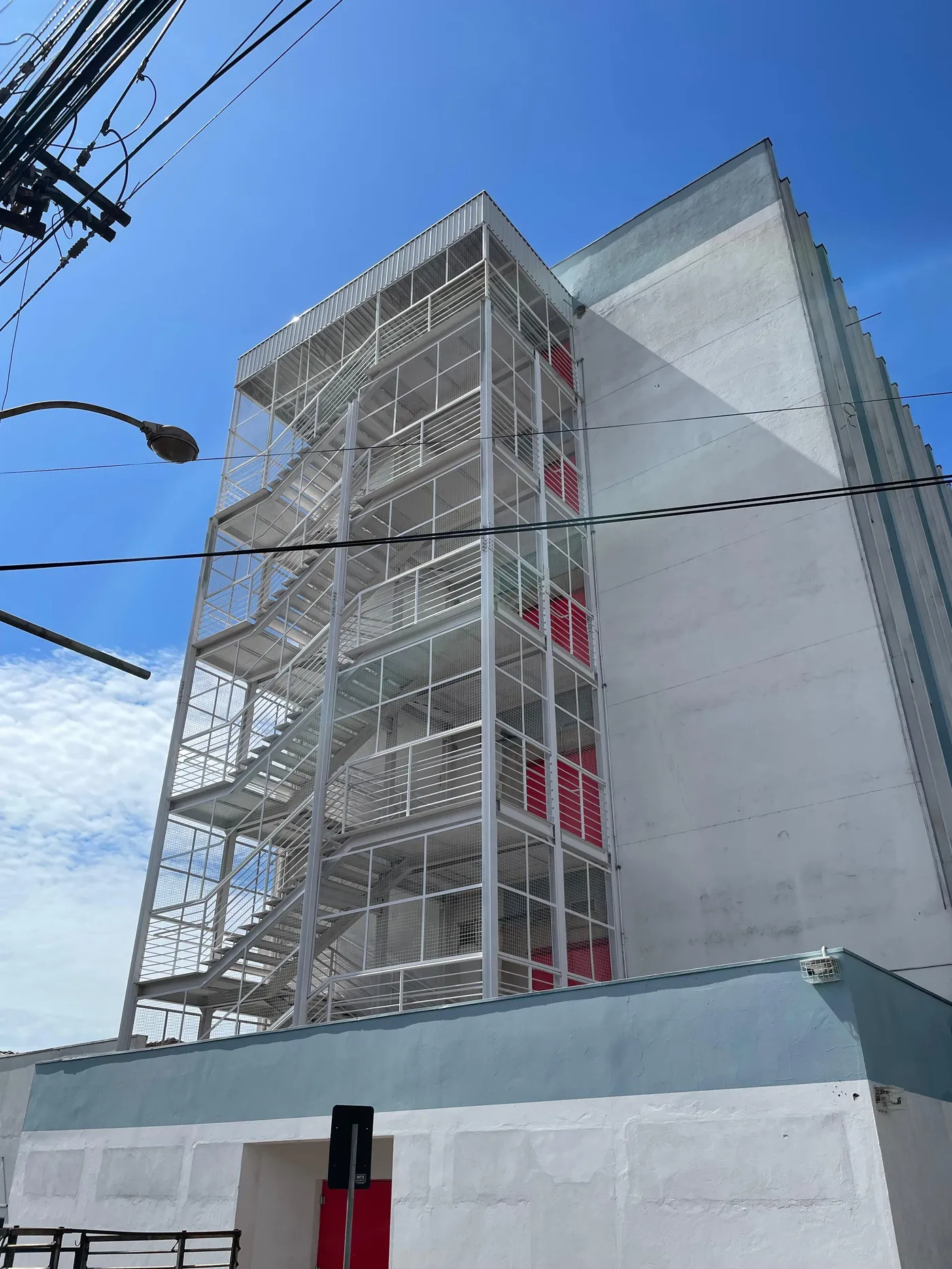 Torre de escada metálica externa em edifício, com guarda-corpo e fechamento em tela